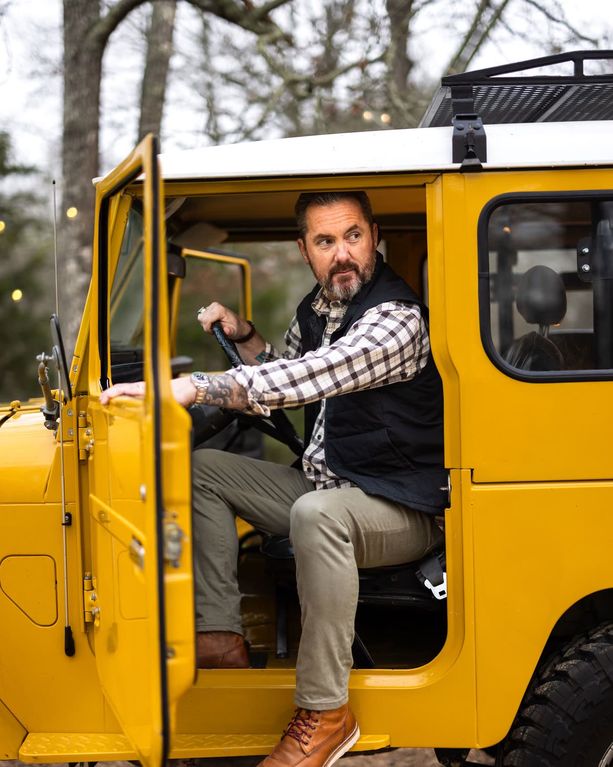 Man in olive chinos seated in the door of a yellow Land Cruiser