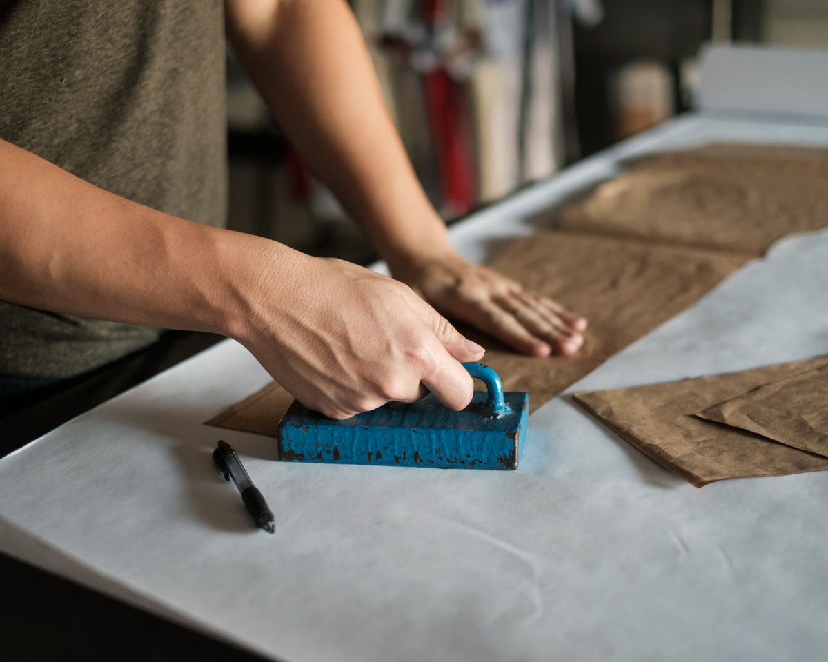 Hands pressing a paper pattern onto tan fabric on the cutting table