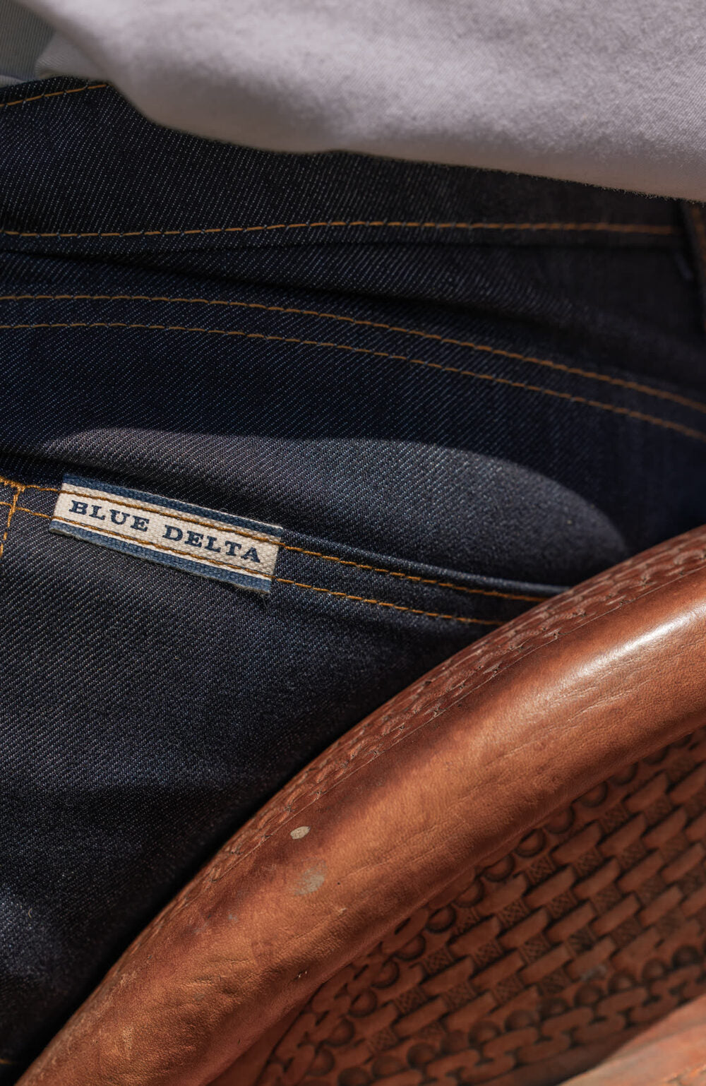 The back pocket and Blue Delta label on dark raw denim, against a leather saddle