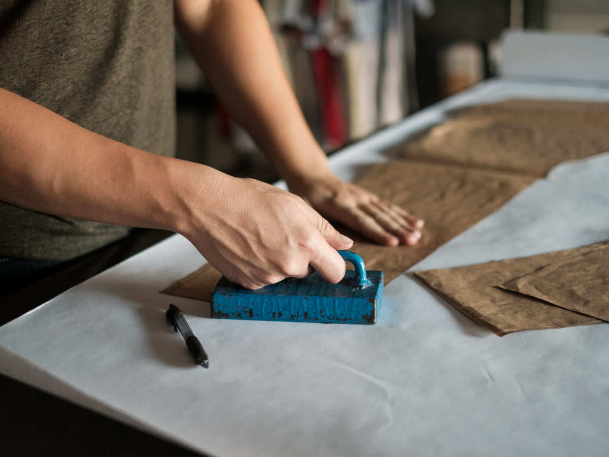 Hands pressing a paper pattern onto tan fabric on the cutting table