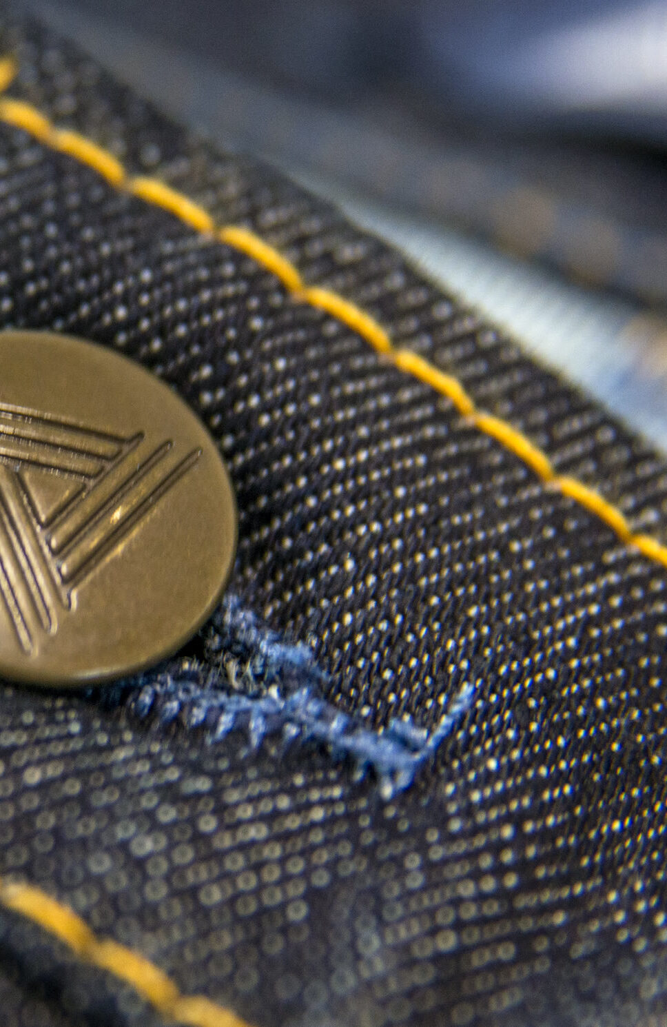 A shank button on raw denim, close up on the stitching