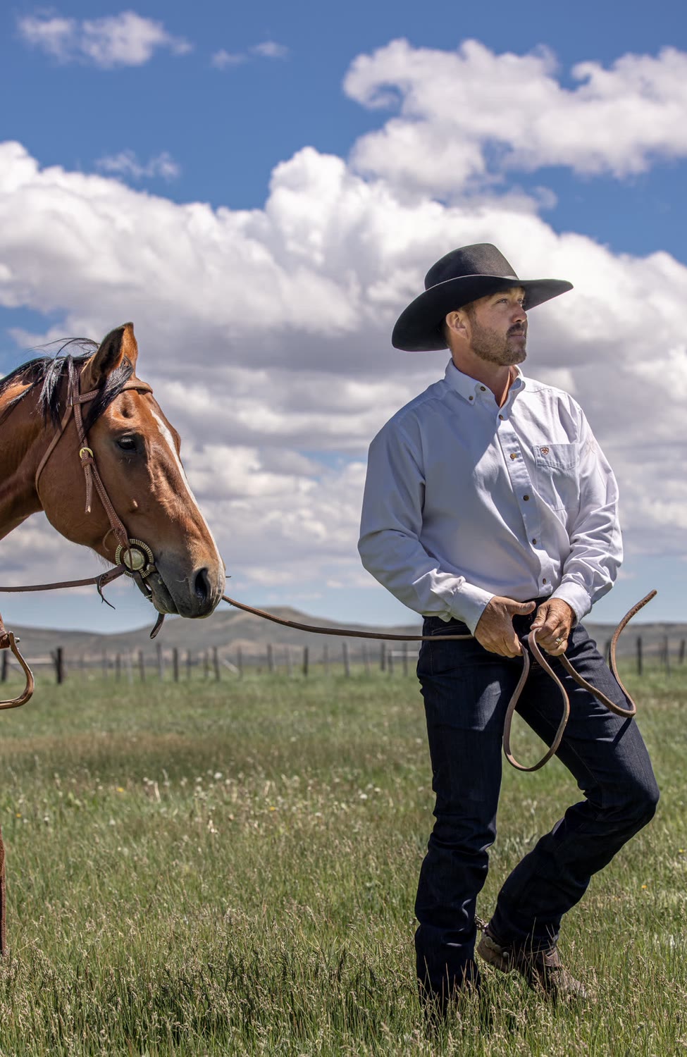 Man in a white shirt and dark jeans leading a horse across a field