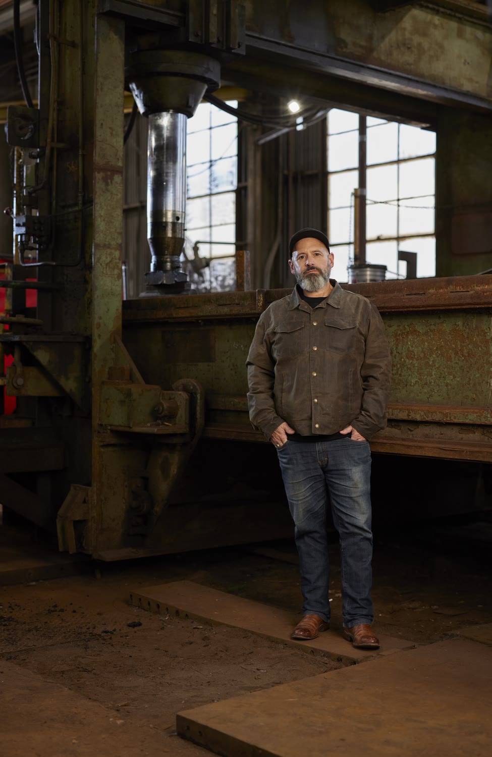Man in a work shirt and dark jeans standing in an old steel forge