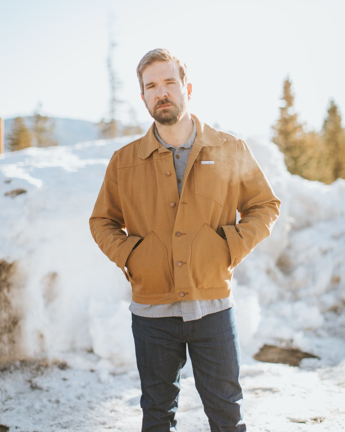 Man in a tan canvas jacket and jeans standing in the snow