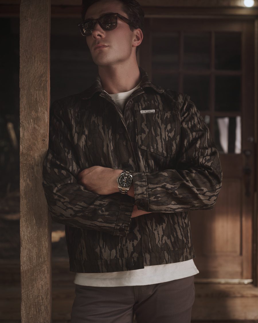 Men's Bottomland canvas jacket worn over a white tee, arms crossed, on a wooden porch.