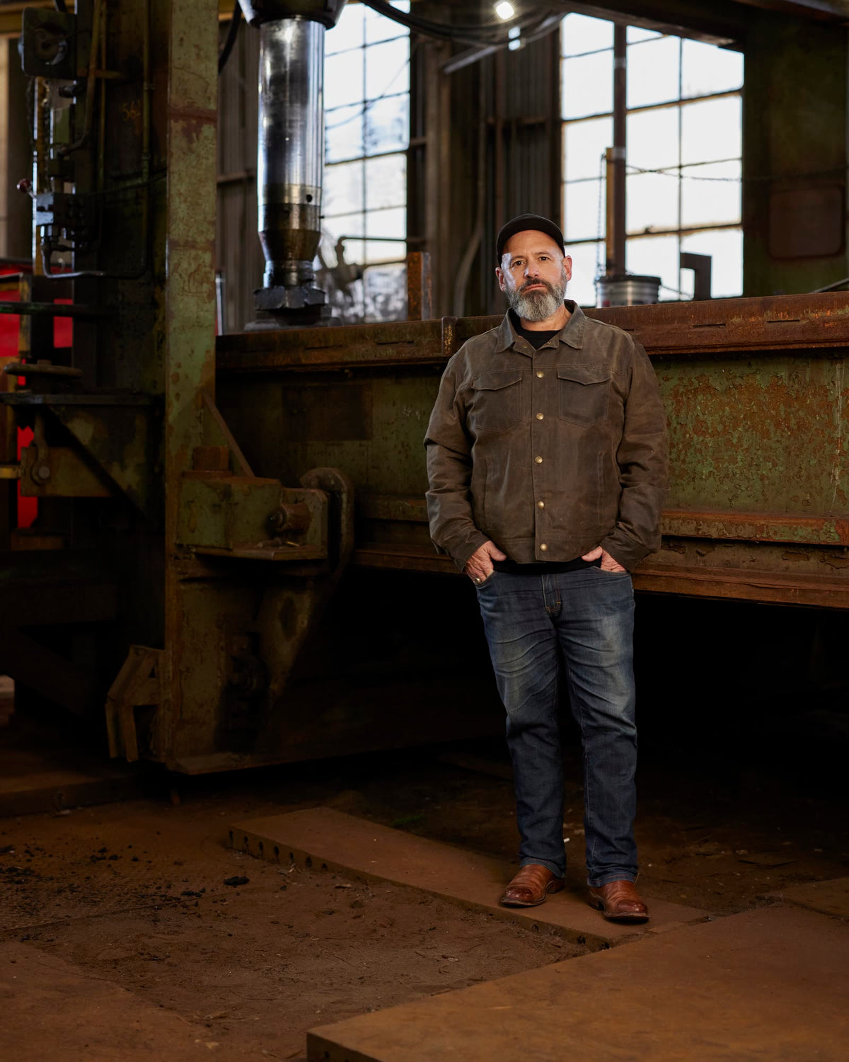 Man in a work shirt and dark jeans standing in an old steel forge
