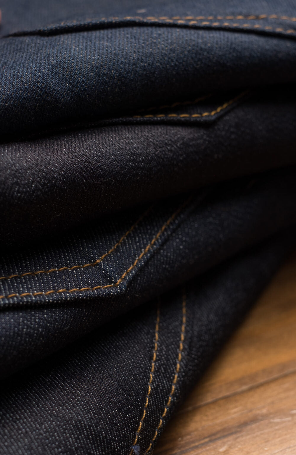 Folded dark raw denim jeans, close up on the stitching