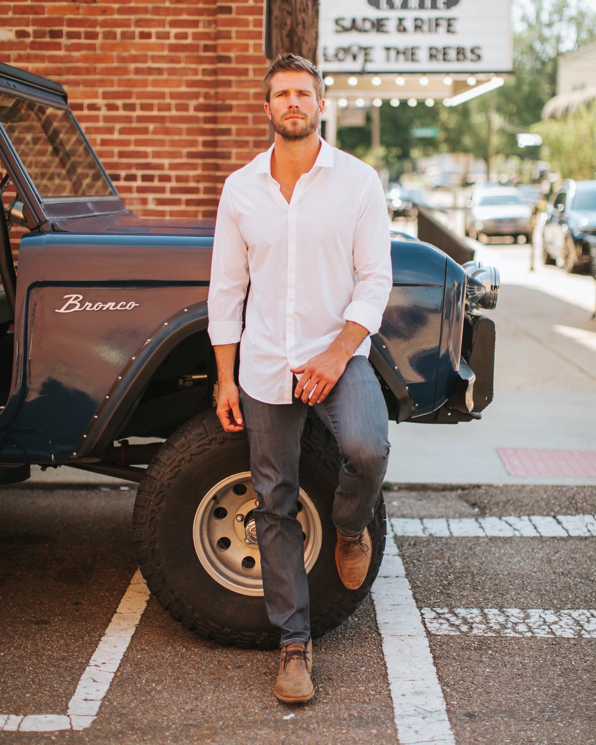Man in a white shirt and dark jeans leaning on a vintage Bronco