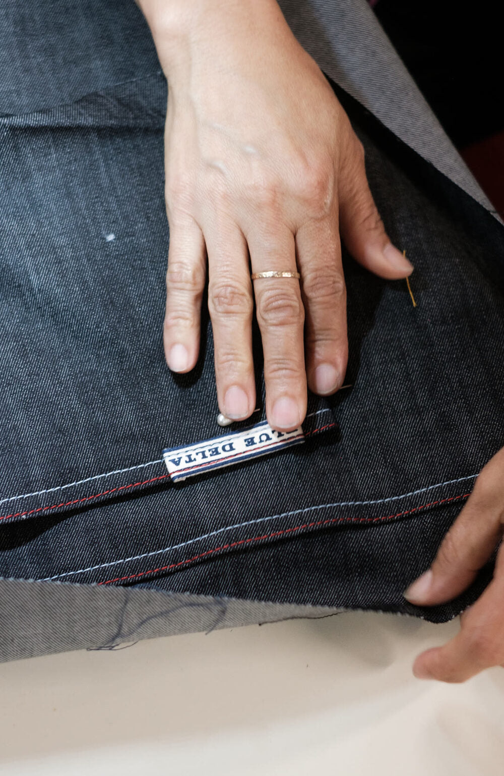 Hands smoothing a panel of raw denim with the Blue Delta label before it is sewn