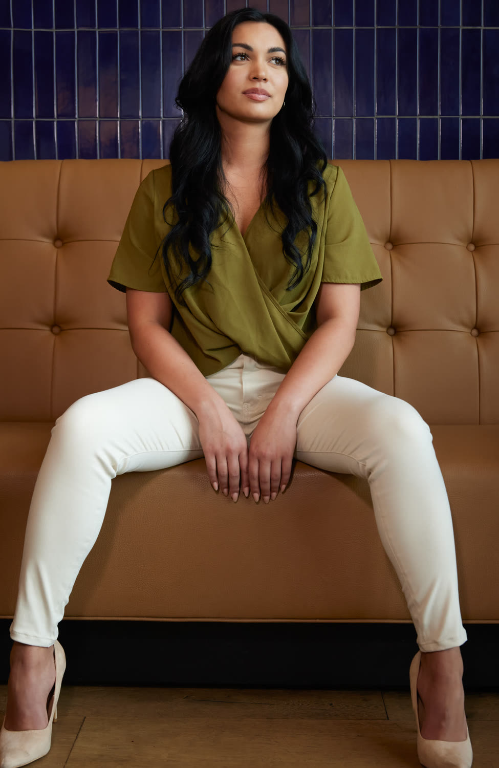 Woman in cream chinos and heels seated on a leather banquette