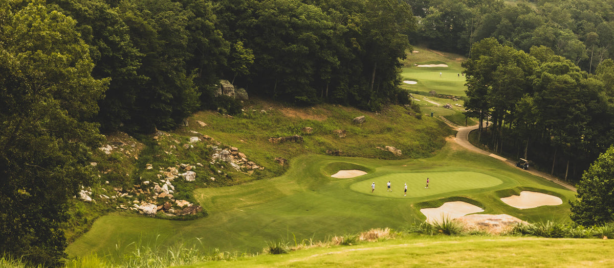 A golf course seen from above, bunkers and fairway between the trees