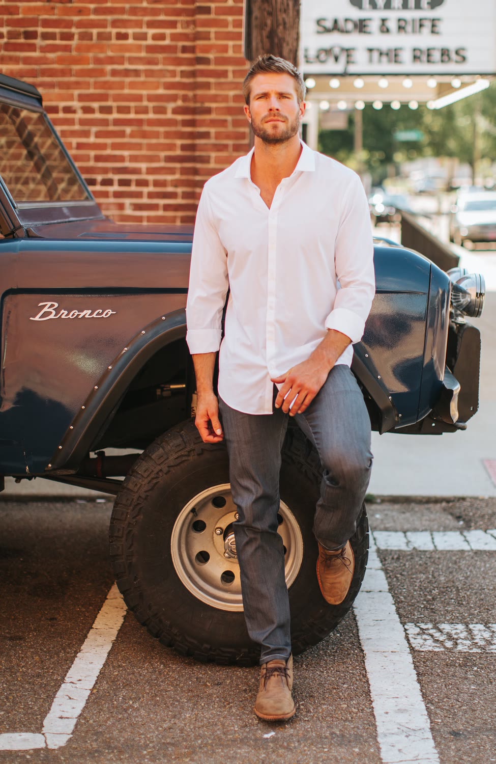 Man in a white shirt and dark jeans leaning on a vintage Bronco