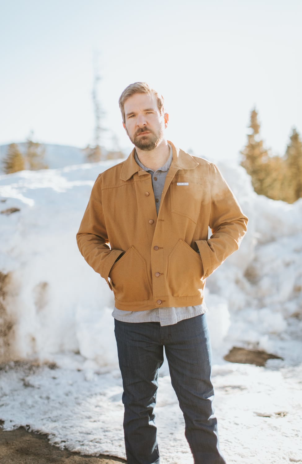 Man in a tan canvas jacket and jeans standing in the snow