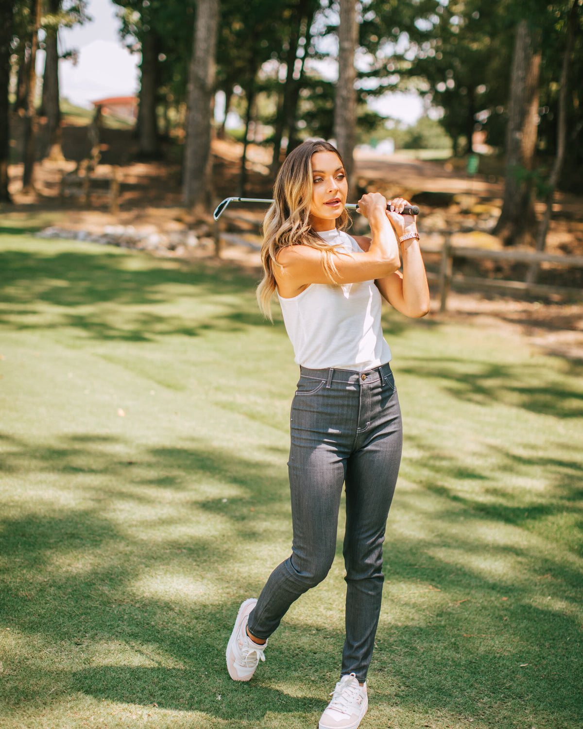 Woman in gray performance pants and a white top finishing a swing on the course