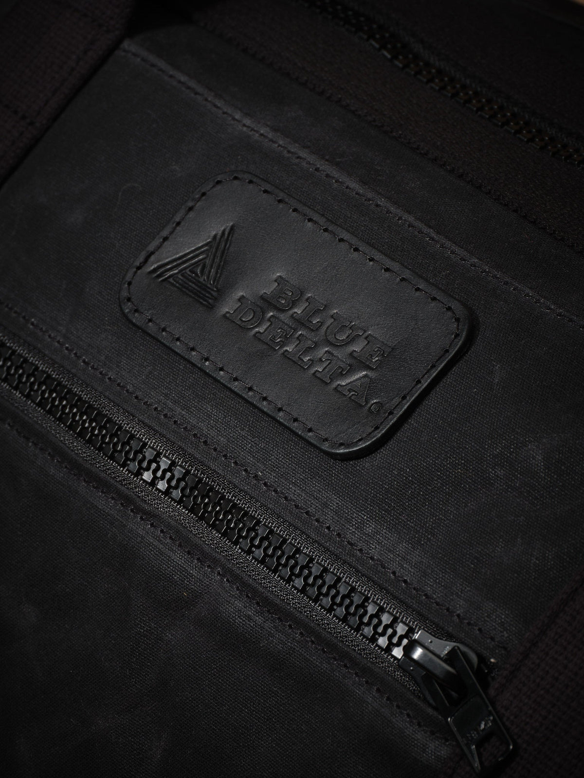Waxed Canvas Duffle in black: leather logo patch and front zipper pocket