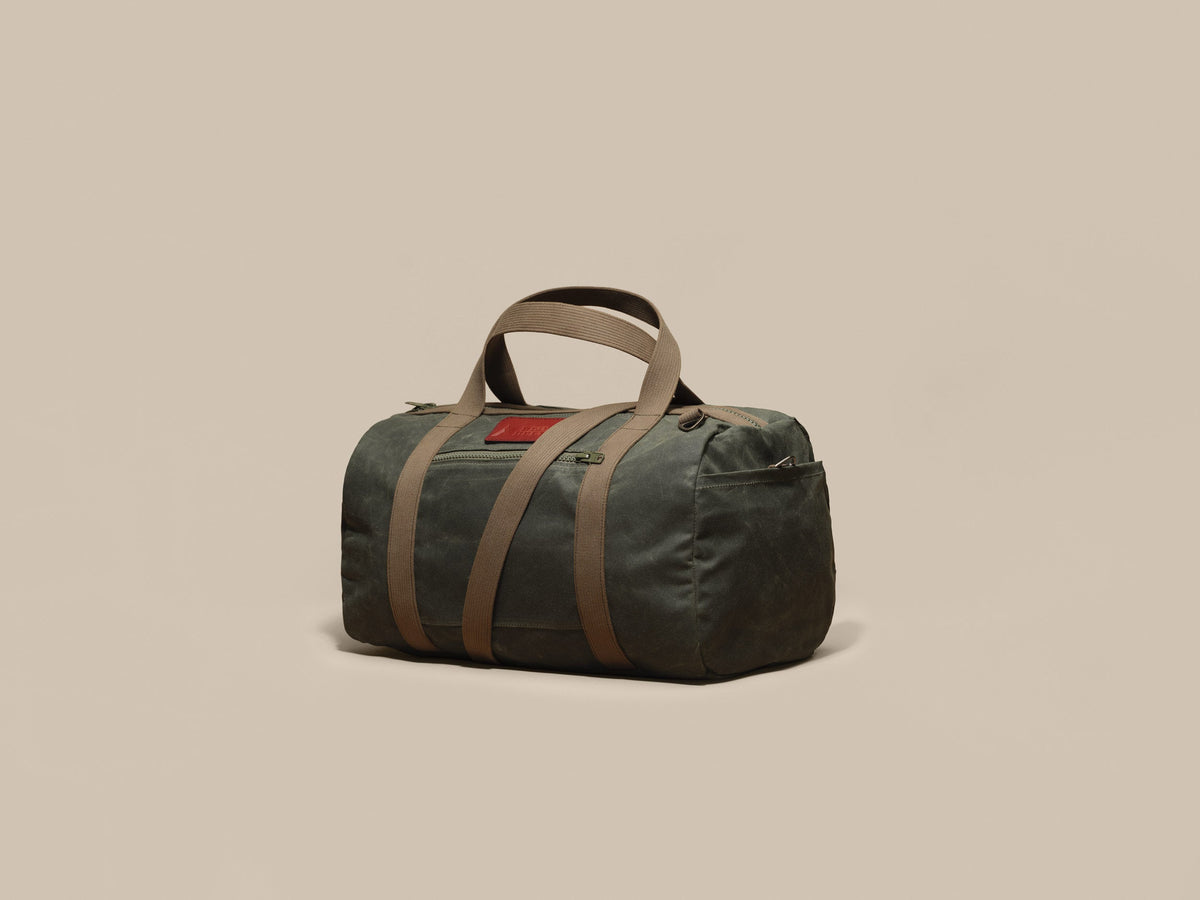 Waxed Canvas Duffle in green waxed canvas with green webbing and a Chestnut leather patch, angled view