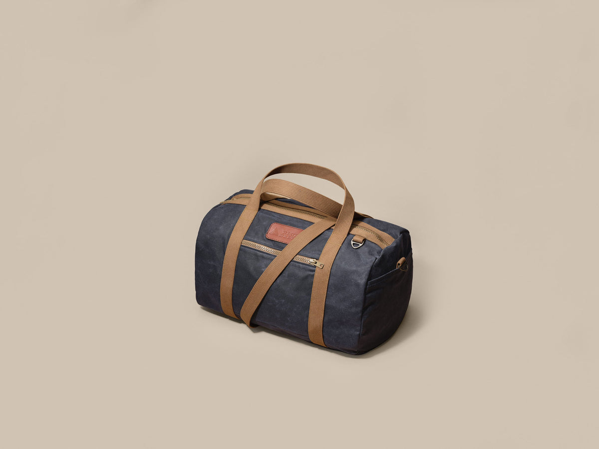 Waxed Canvas Duffle in navy waxed canvas with tan webbing and a Rich Brown leather patch, three-quarter view