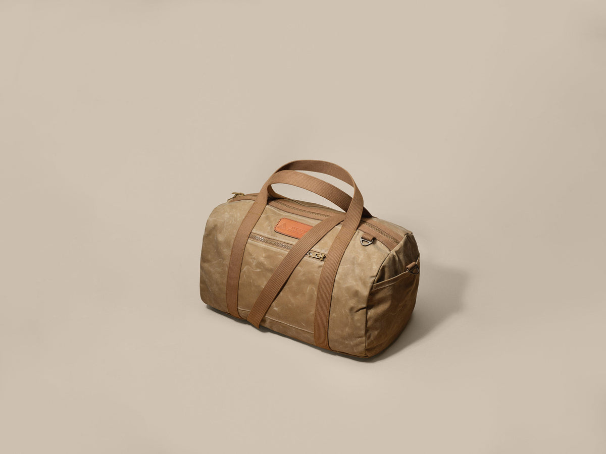Waxed Canvas Duffle in tan waxed canvas with tan webbing and a Gold Brown leather patch, angled view