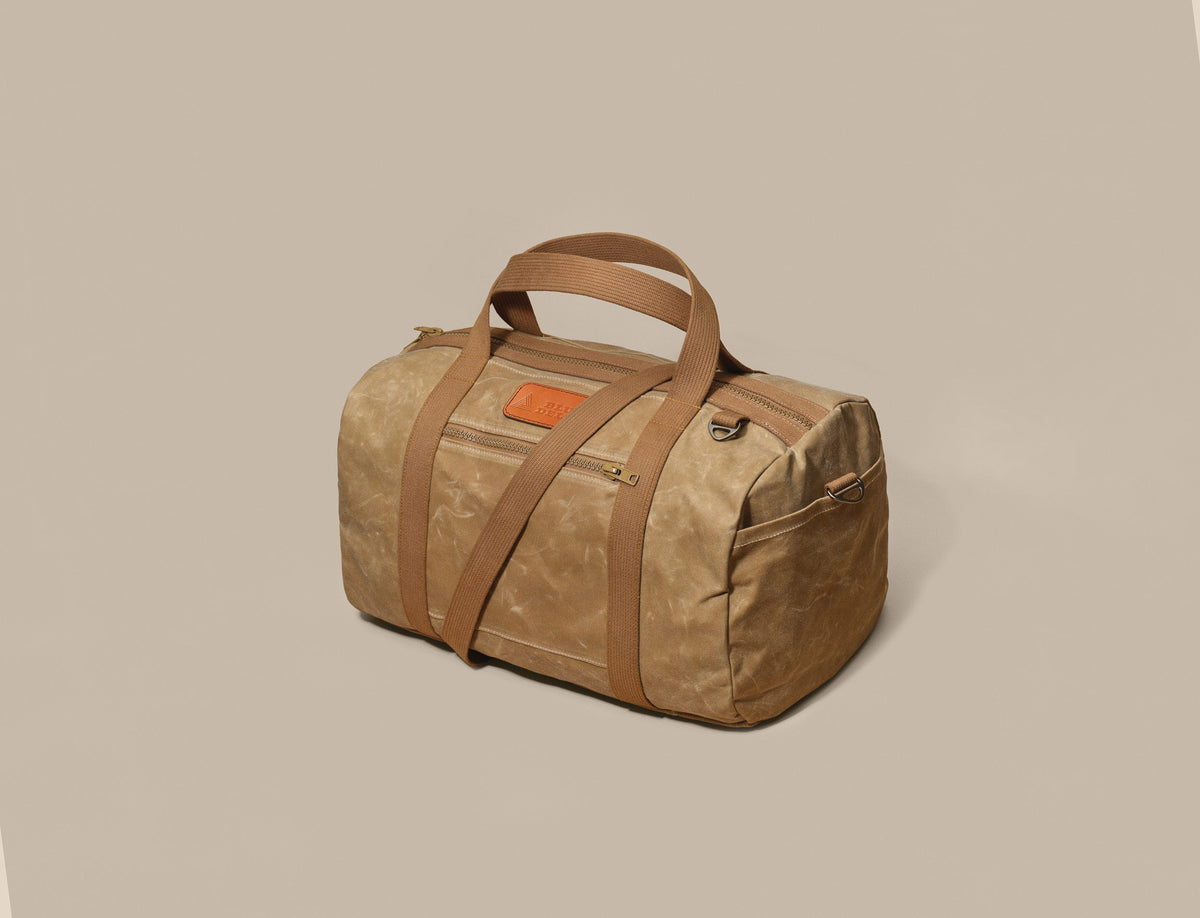 Waxed Canvas Duffle in tan waxed canvas with tan webbing and a Gold Brown leather patch, three-quarter view
