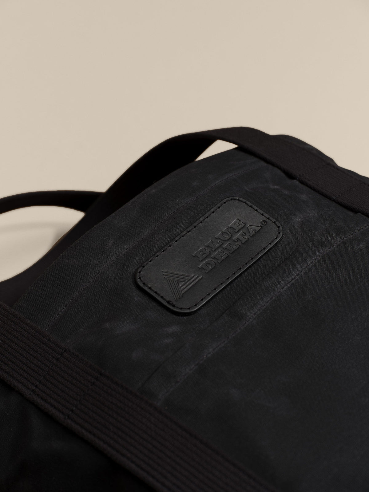 Waxed Canvas Tote in black: leather logo patch close-up