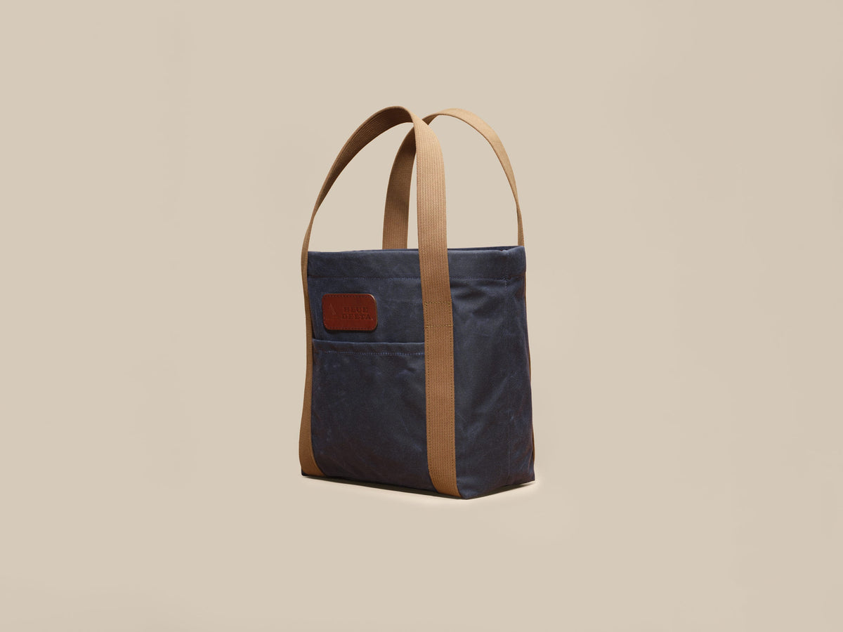 Waxed Canvas Tote in navy waxed canvas with tan webbing and a Rich Brown leather patch, angled view