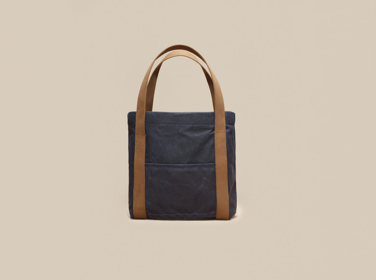 Waxed Canvas Tote in navy waxed canvas with tan webbing and a Rich Brown leather patch, slip pocket side