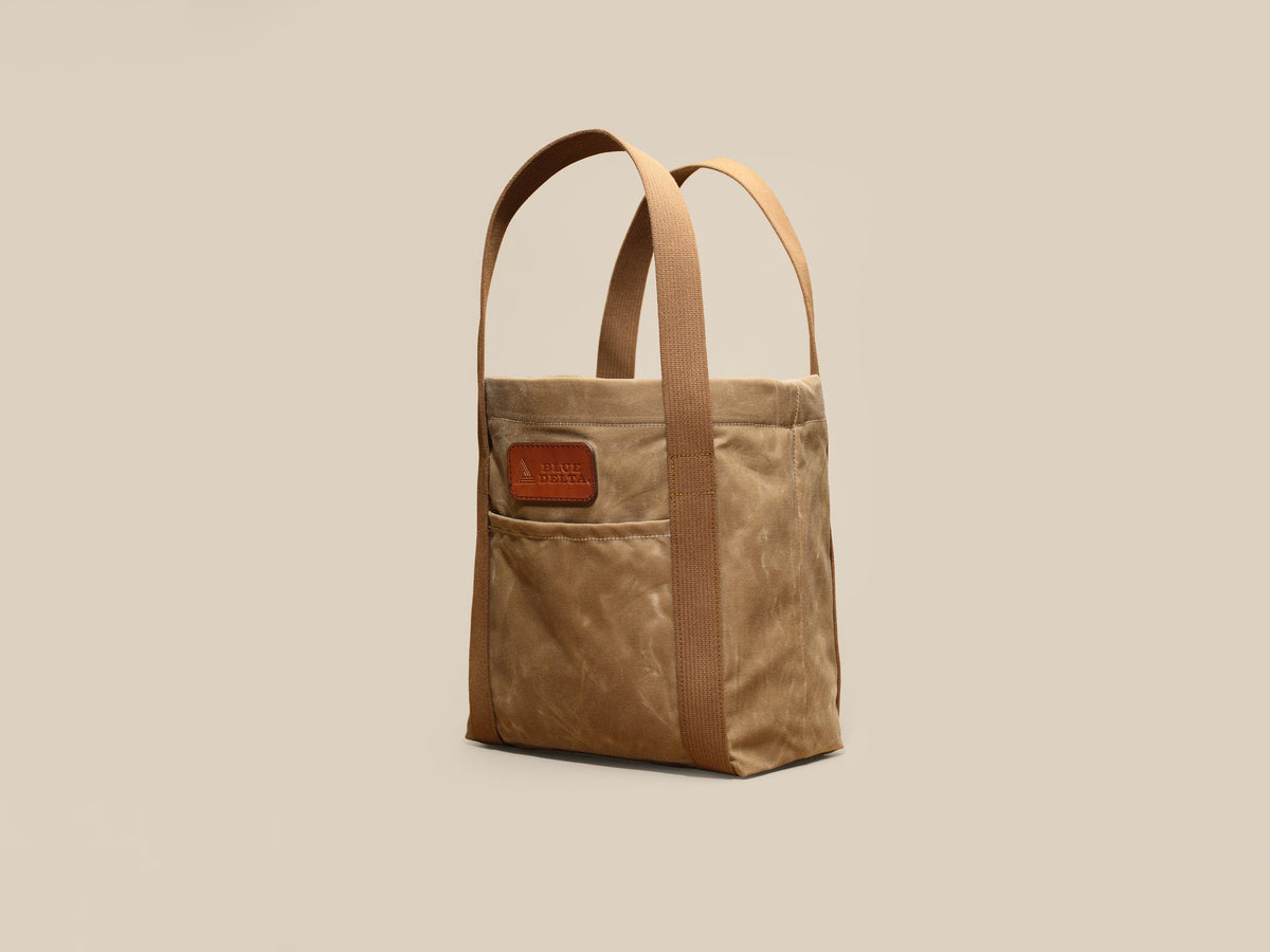 Waxed Canvas Tote in tan waxed canvas with tan webbing and a Gold Brown leather patch, angled view